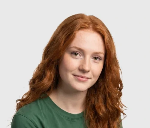 Young woman with long curly red hair wearing a green shirt, smiling softly against a plain background.