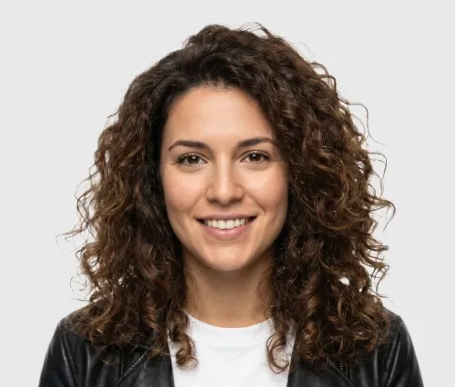 Smiling woman with curly brown hair wearing a black leather jacket and white shirt.