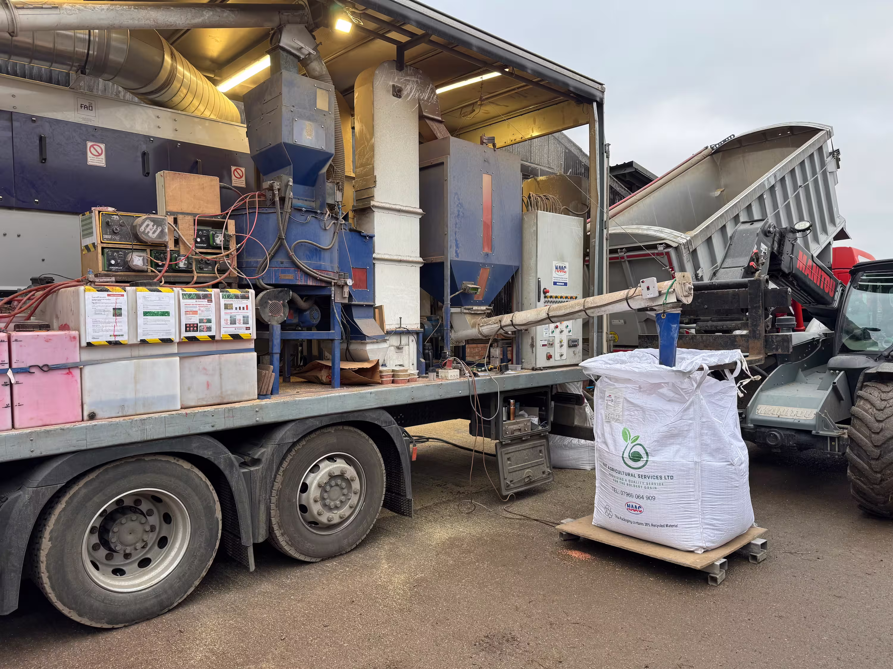 Mobile agricultural processing machine on truck loading grain or seed into large white bag outdoors.