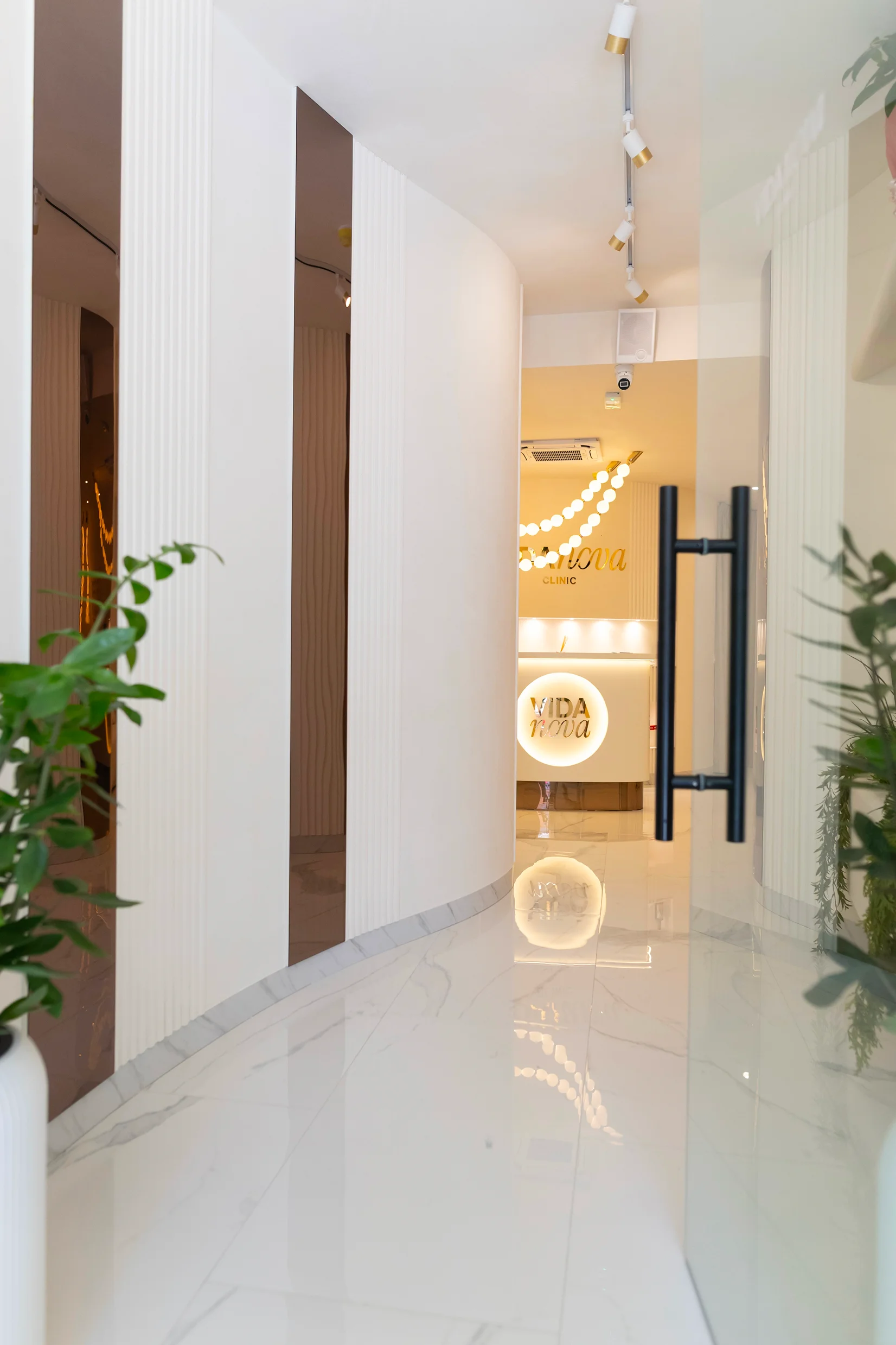 Modern beauty salon reception with white counter, floral decor, round lights, and cozy seating area.