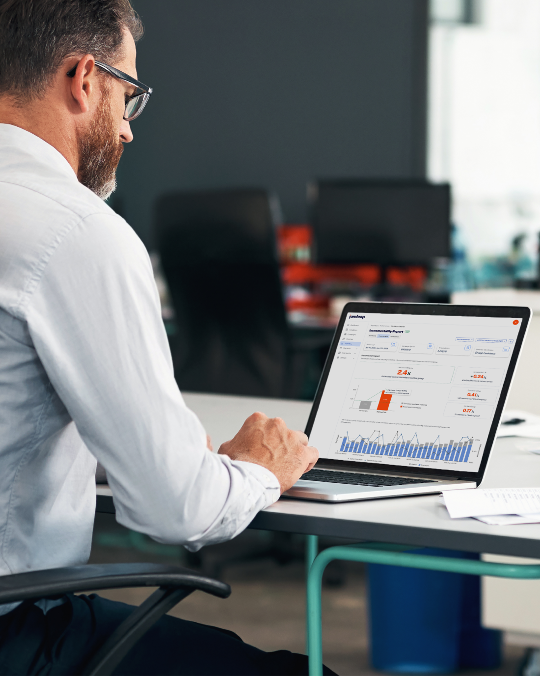 Man in white shirt sitting at a desk working on a laptop displaying a performance report with charts.