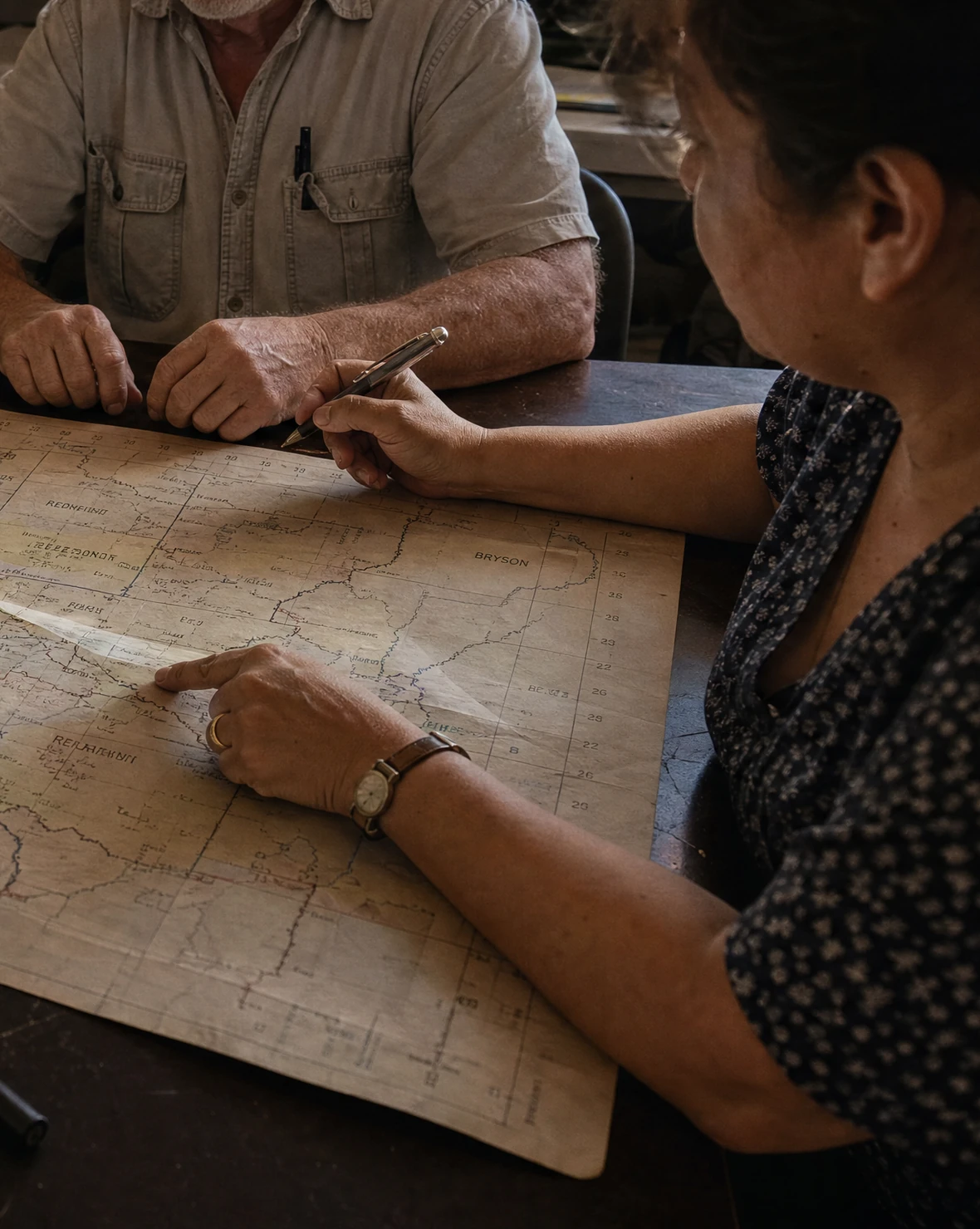 A media planner tracing a county boundary on a printed map beside a laptop