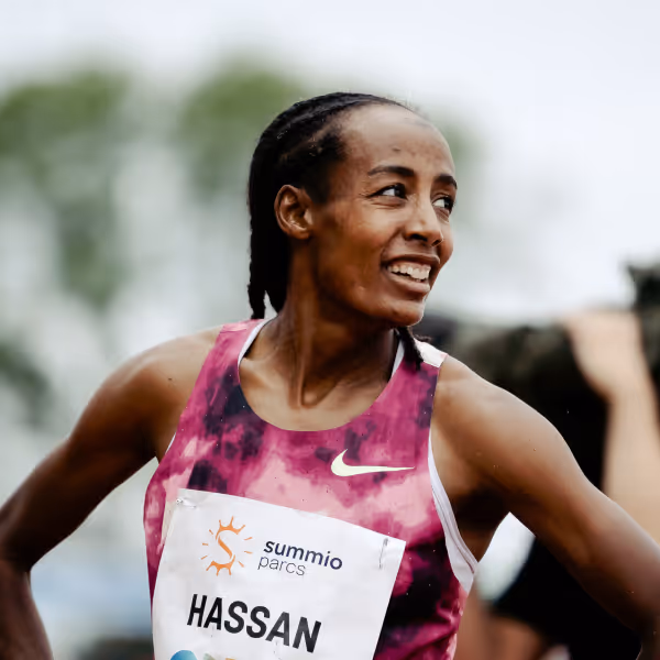 Sifan Hassan with braided hair smiling and wearing a pink Nike sports top with a race bib.