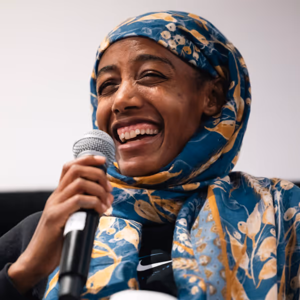 Smiling Sifan Hassan wearing a patterned blue and yellow headscarf holding a microphone.