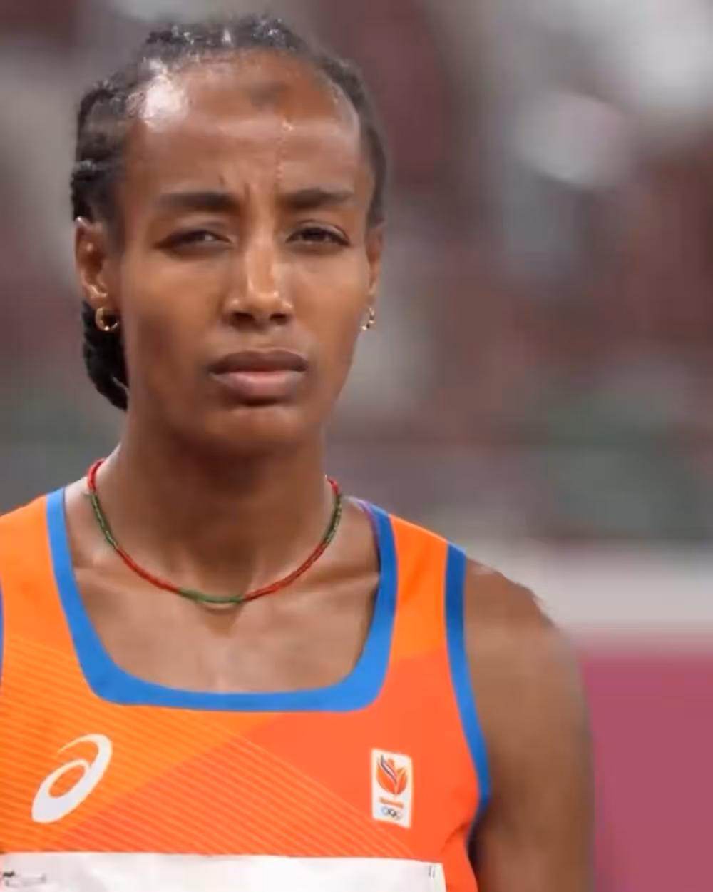 Female athlete in orange and blue sportswear with braided hair and focused expression.