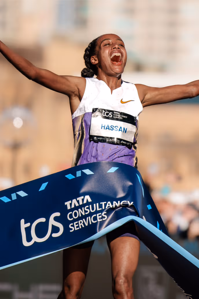 Runner Hassan crossing the finish line with arms raised in celebration at a marathon event.