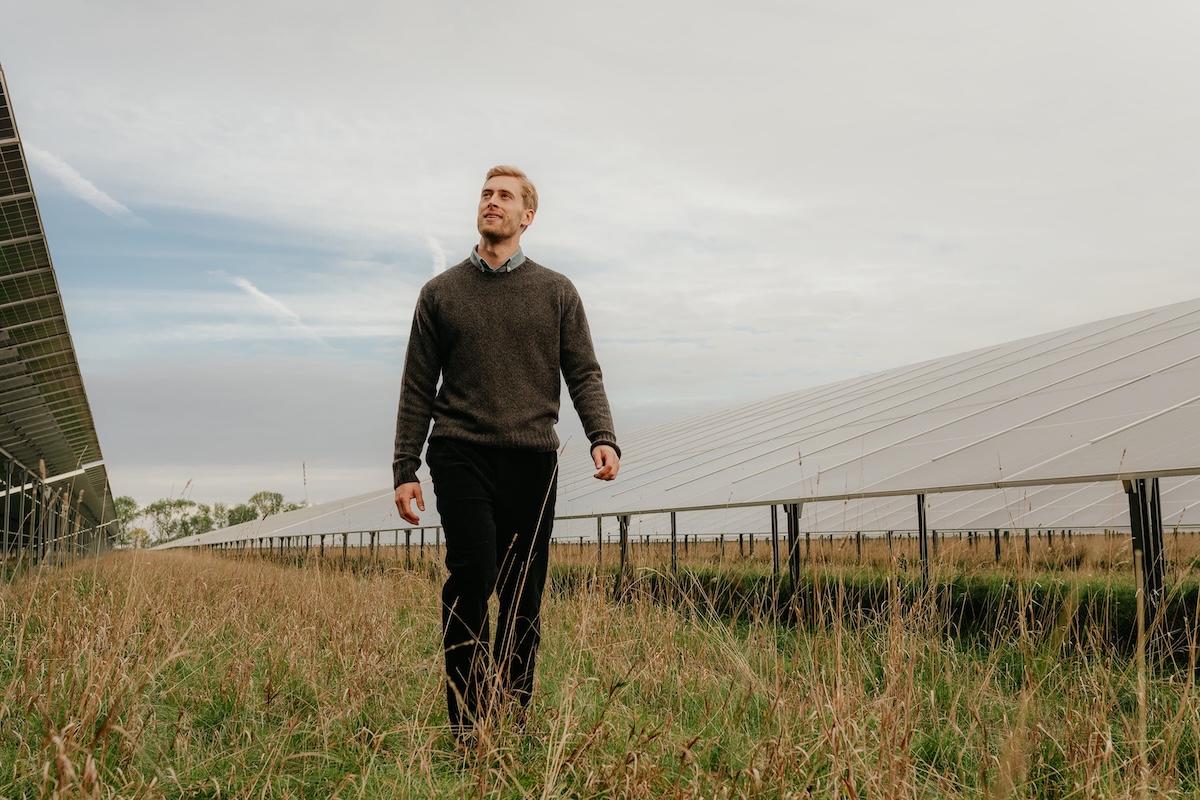 Ein Mann geht durch ein Feld mit Solarpanels auf beiden Seiten bei bewölktem Himmel.