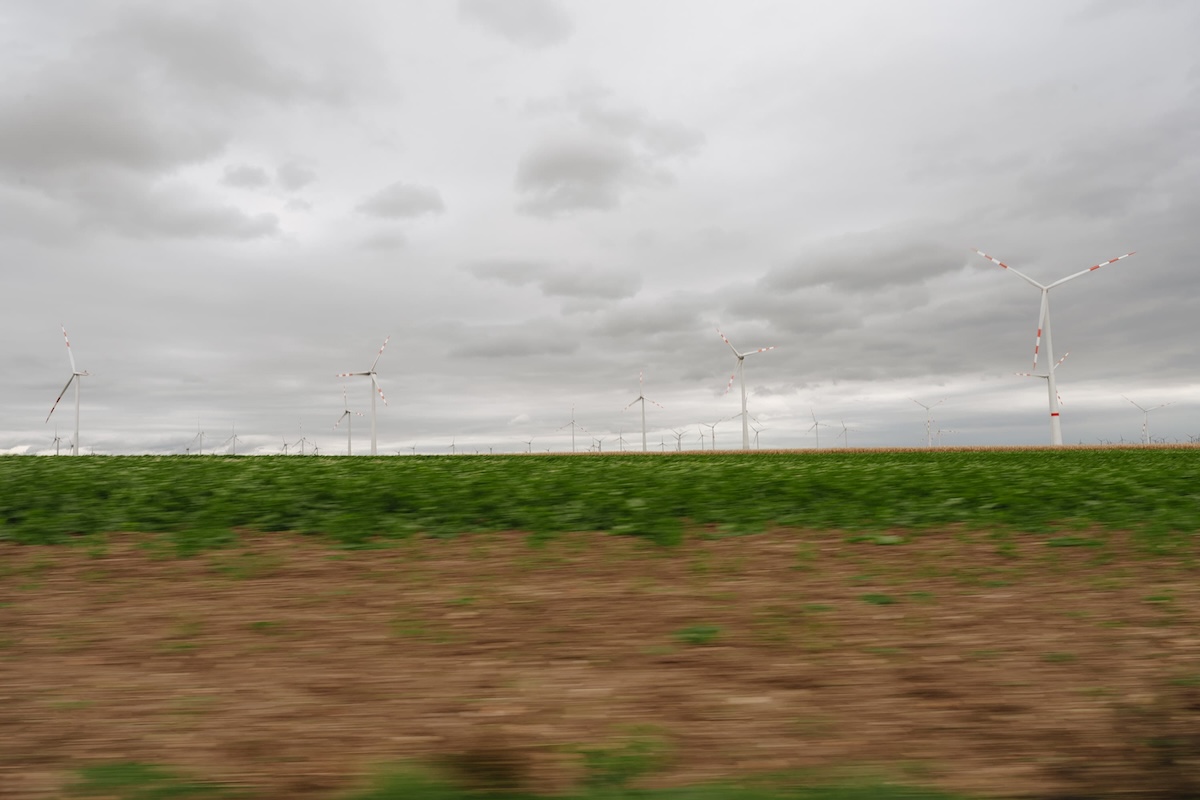 Mehrere Windräder stehen in einer grünen Landschaft unter bewölktem Himmel.