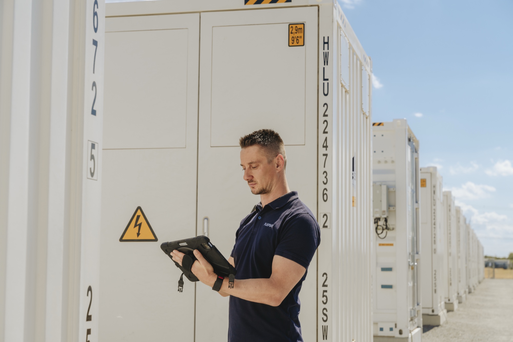 Techniker steht vor weißen Energiespeichercontainer und arbeitet an einem Tablet.