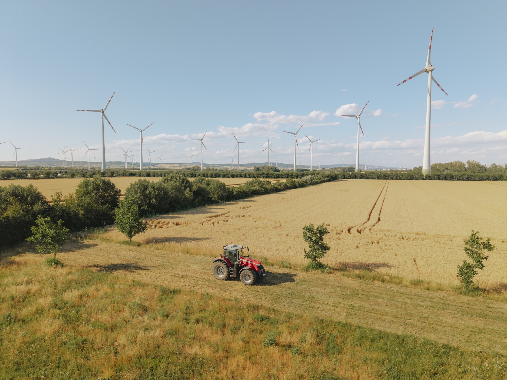 Traktor auf Feld mit Getreide, Windkraftanlagen und blauem Himmel im Hintergrund.