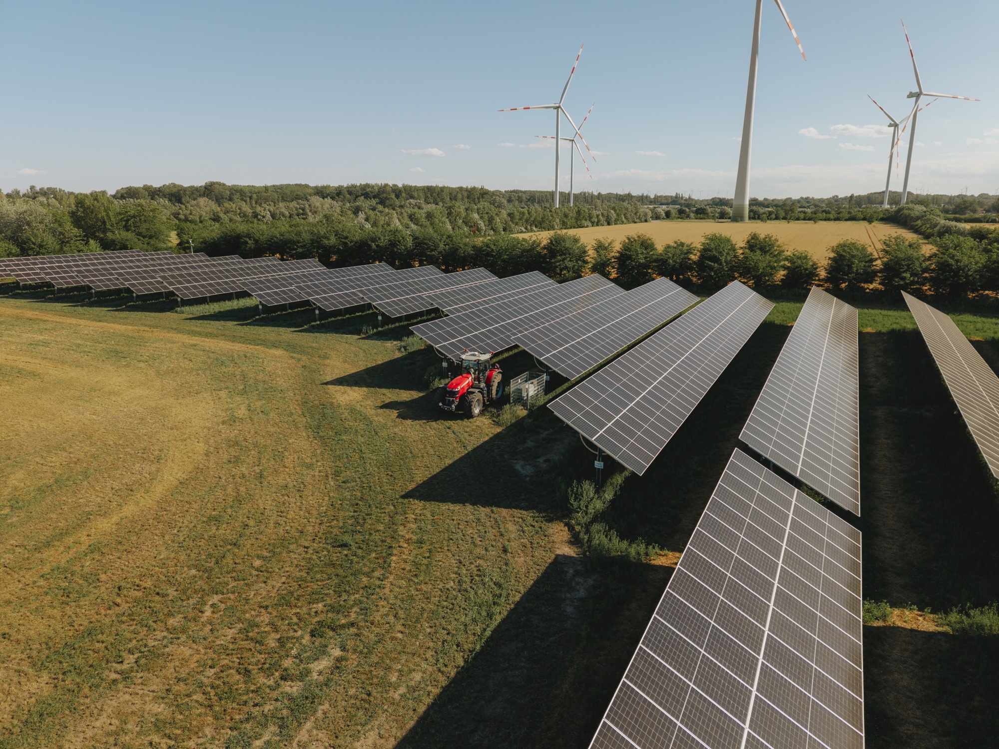 Photovoltaikanlage mit einem Traktor auf Feld, Windräder im Hintergrund unter klarem Himmel.