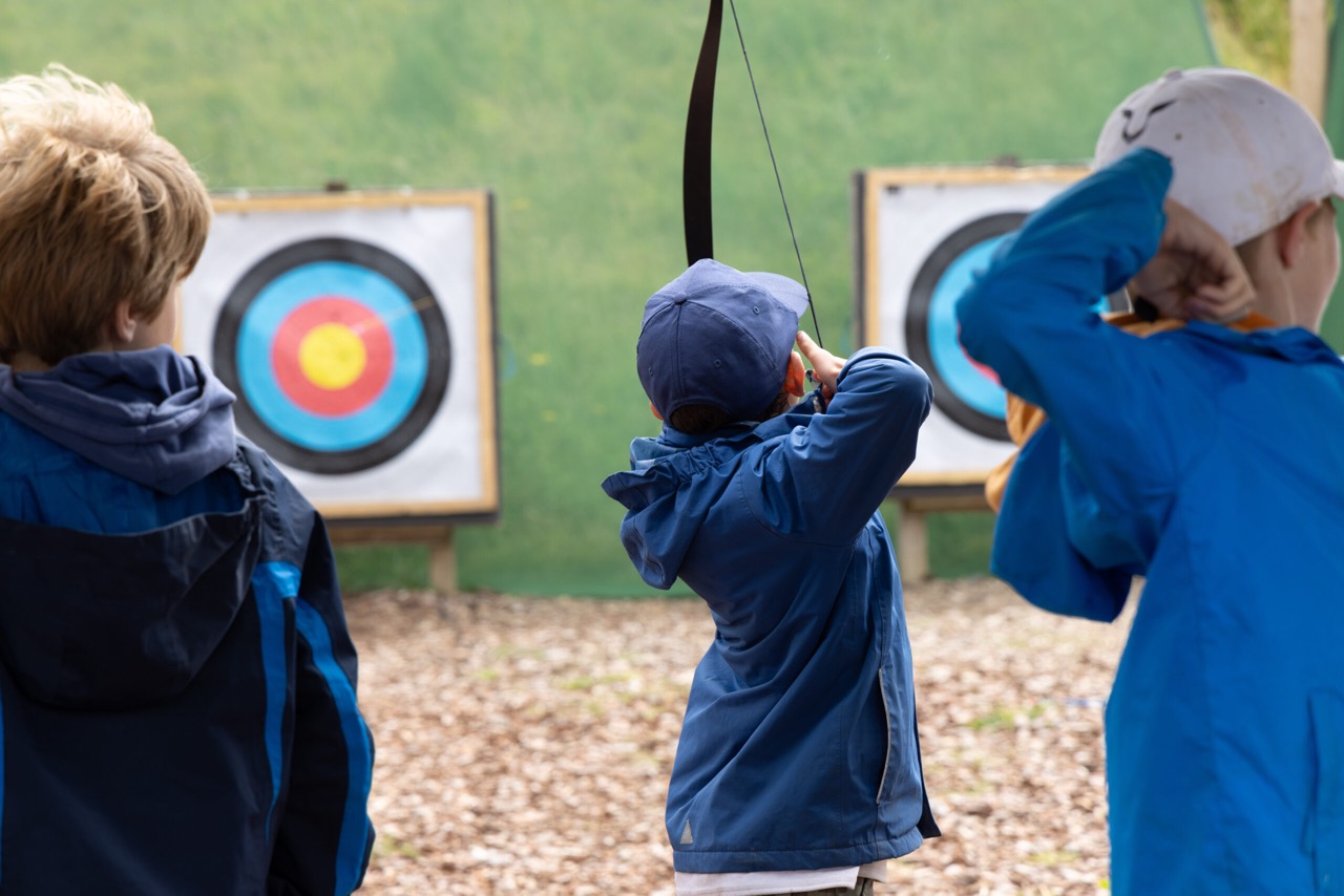 Three children practicing archery aiming at targets with colorful bullseyes.