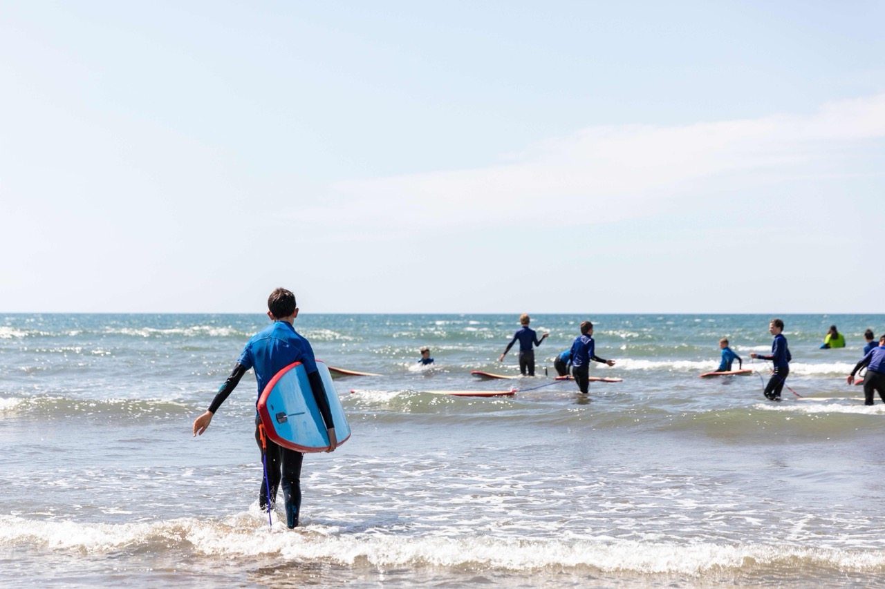 Group of people in wetsuits preparing to surf in the ocean on a sunny day.