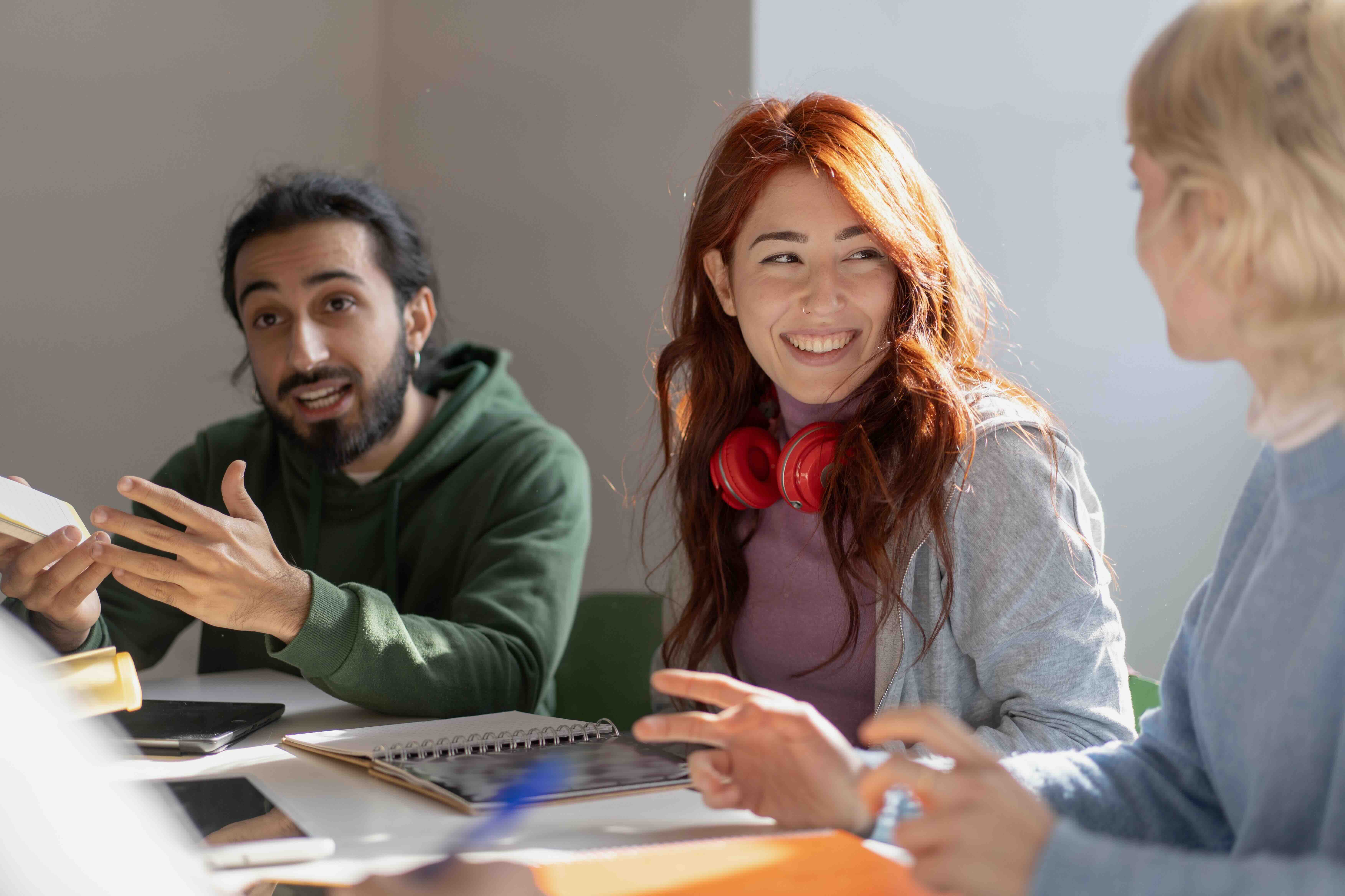 Three young adults having an engaged discussion around a table with notebooks and tablets.