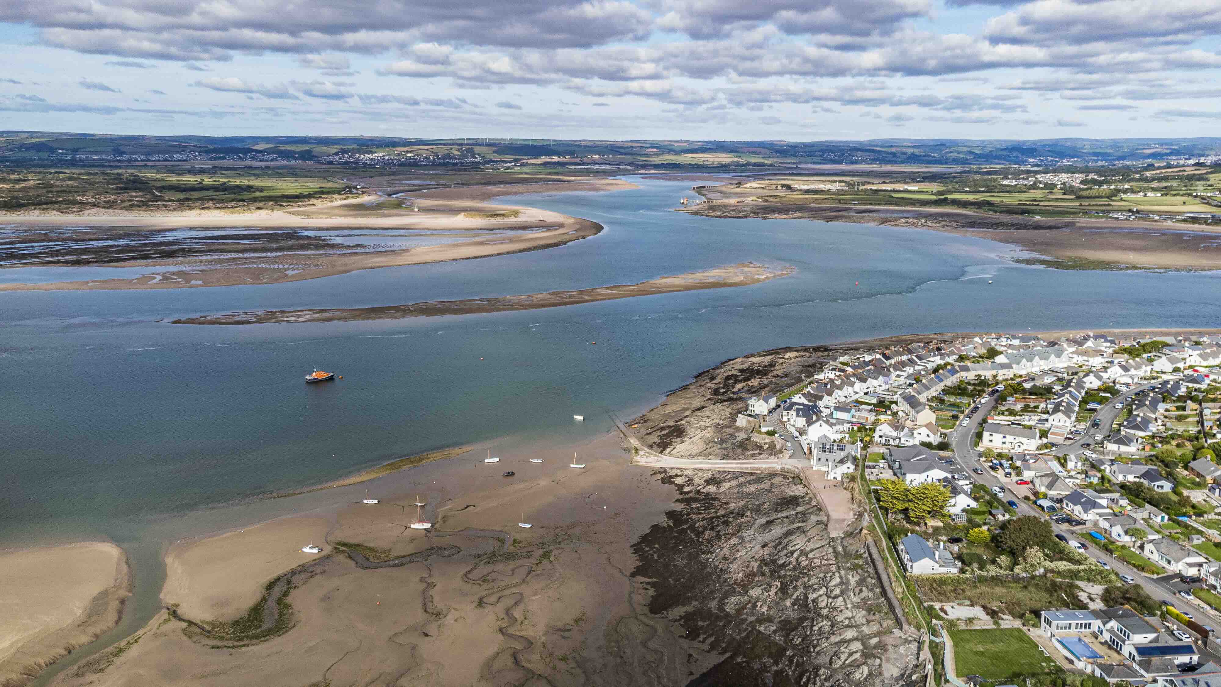 Aerial view of a coastal town by tidal estuary with boats moored on sandbanks under a cloudy sky.