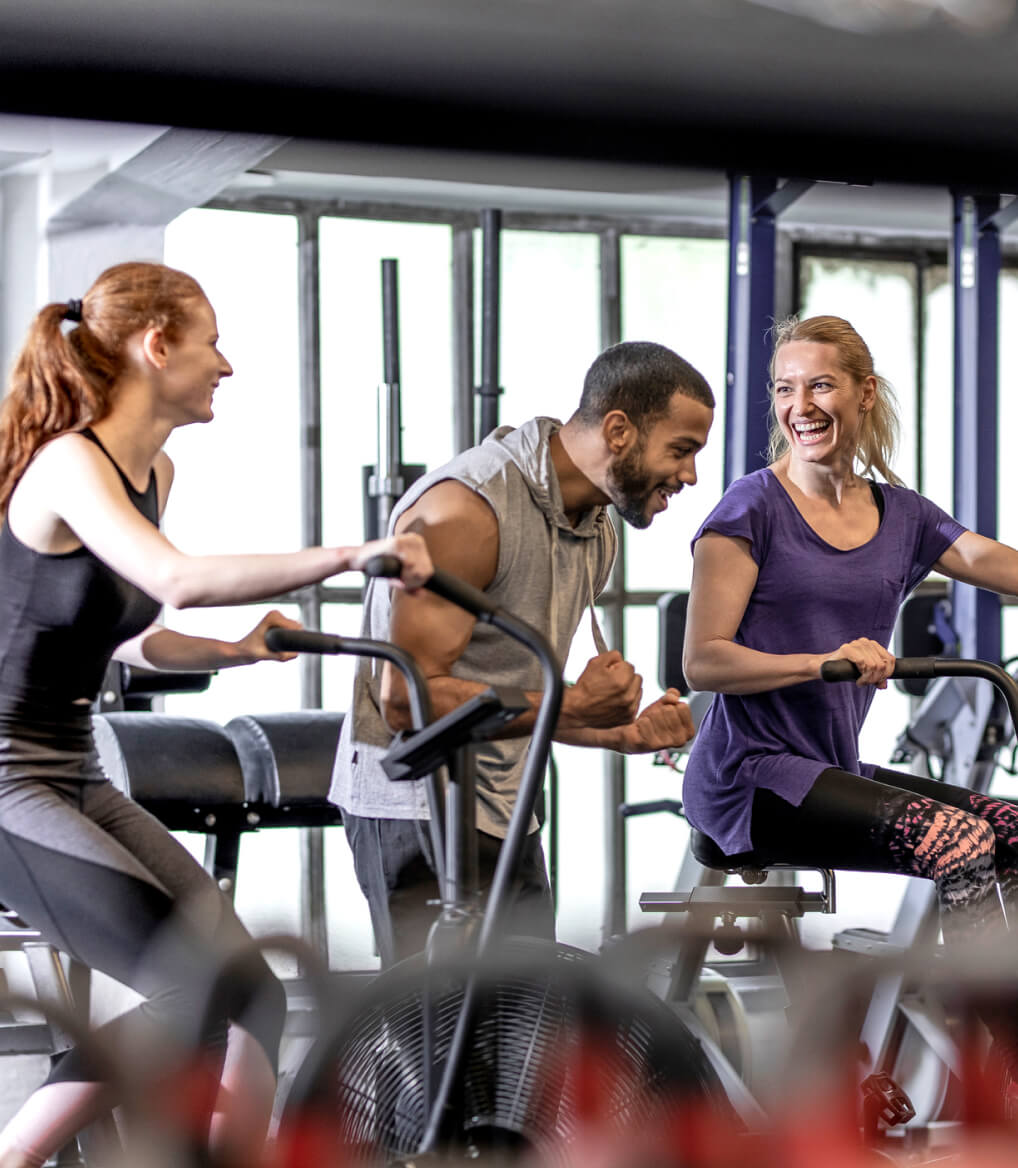 Two women and one man engaging in a lively indoor cycling workout at a gym.