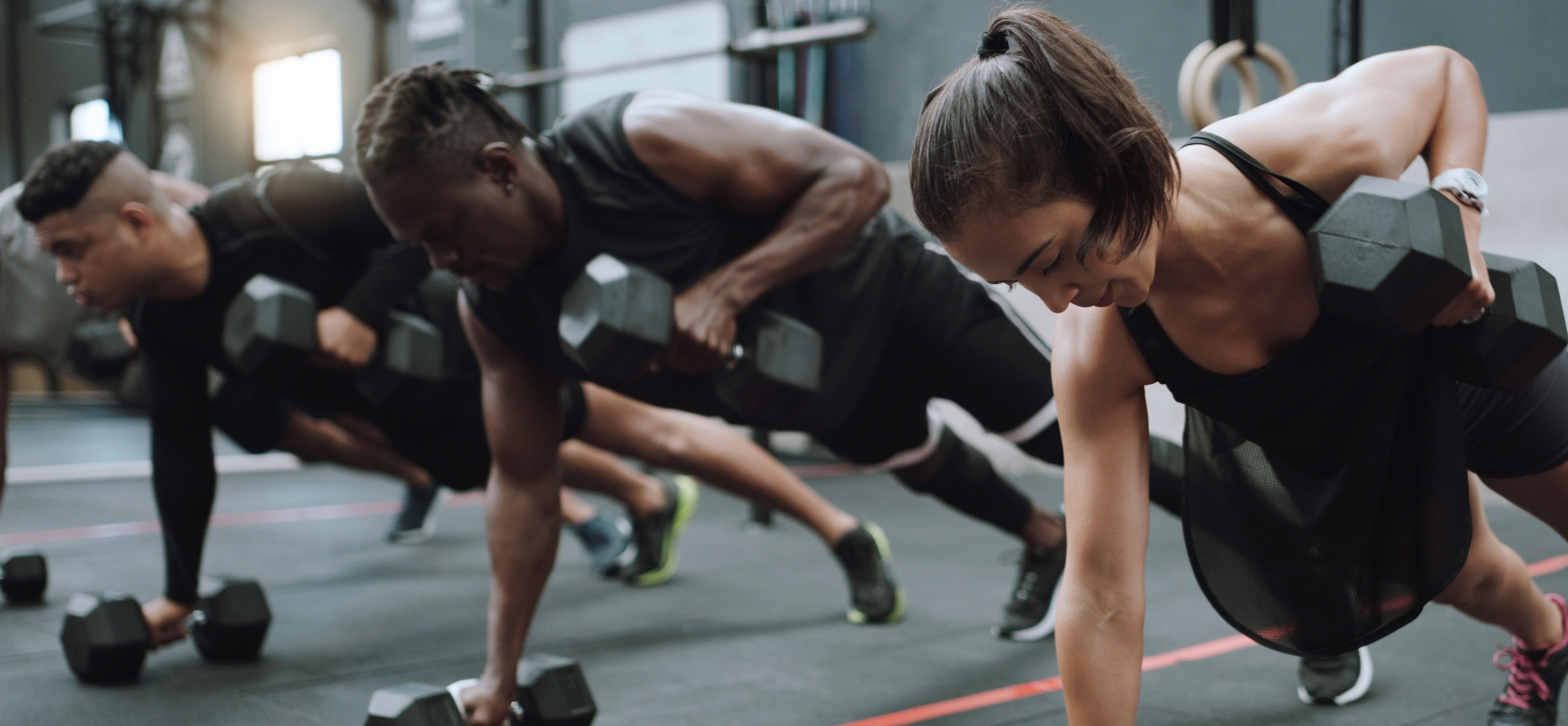 A row of athletes holding a plank with one hand on a dumbbell during a class