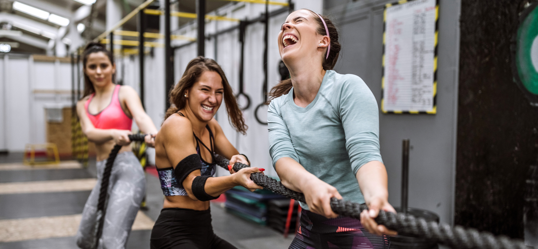 Three women laughing as they pull a battle rope in a functional fitness gym
