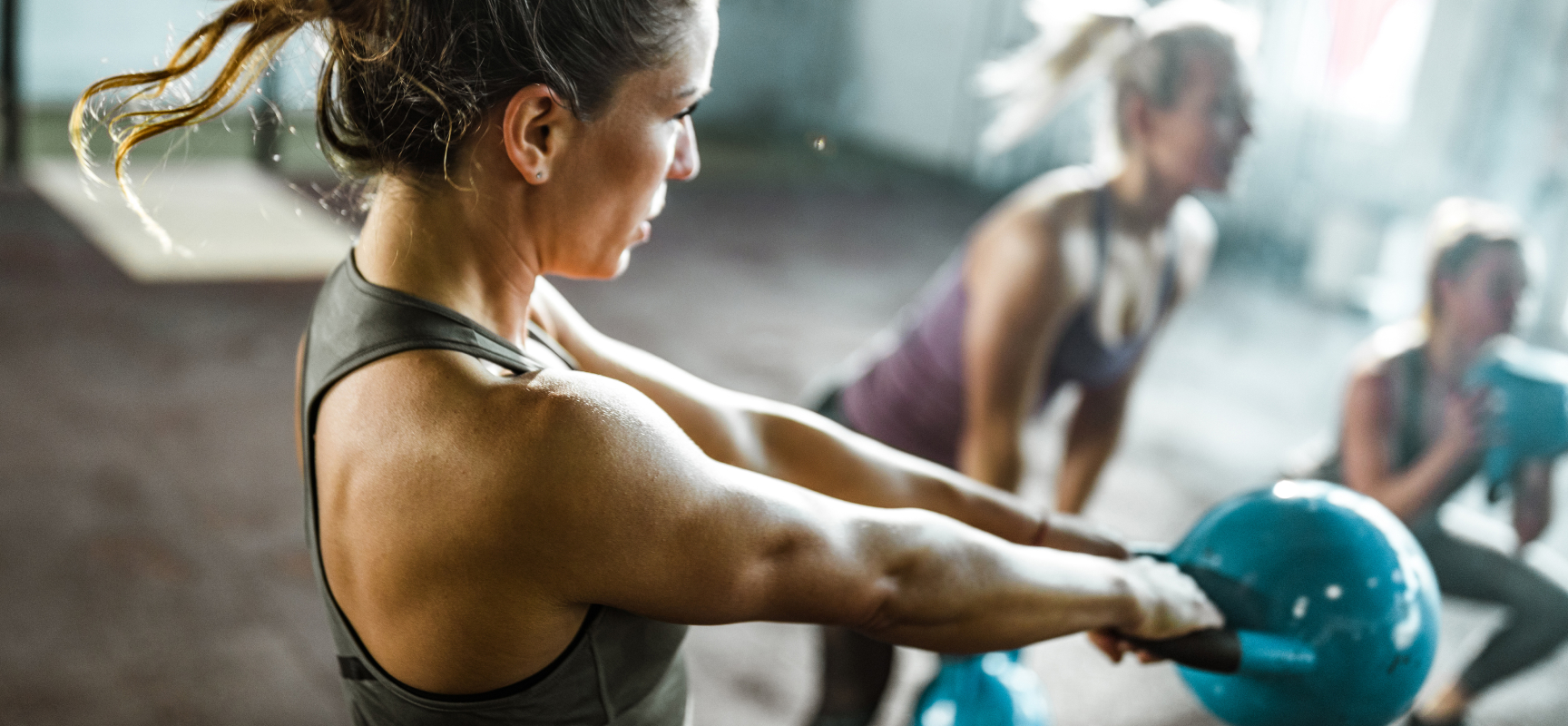 A woman swings a kettlebell in a group fitness class