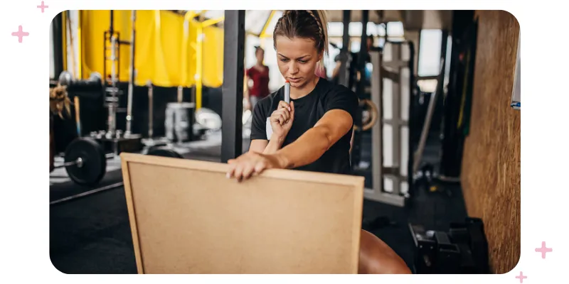 A woman at the gym holding a whiteboard and thinking about what she's going to write.