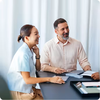 Two professionals, a woman and a man, smiling and engaged in a discussion at a desk with documents and a tablet.