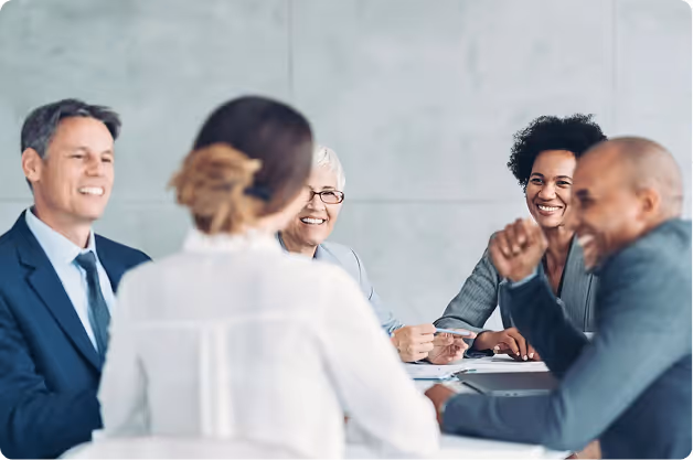 A diverse group of five business professionals smiling and engaged in a meeting around a table.