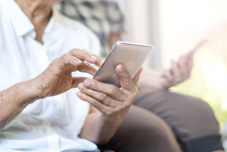 Close-up of an older adult's hands using a smartphone while seated.