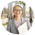 Femme souriante portant des lunettes et tenant un dossier blanc à l'intérieur.