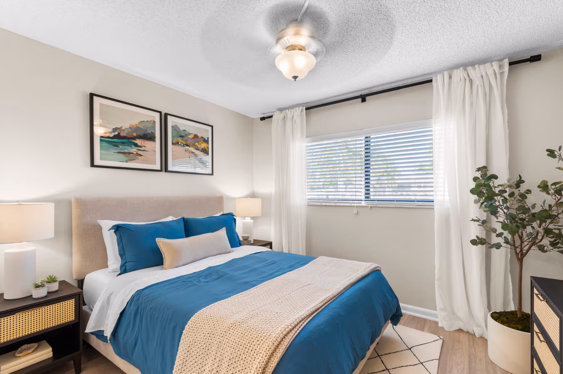 Bedroom with bed, plant, bedside table with lamp, wall art, and large window