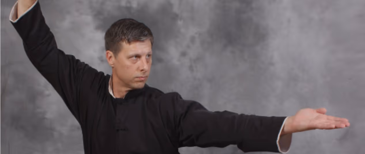Man in black martial arts uniform posing with arms extended, one raised and one palm facing up.