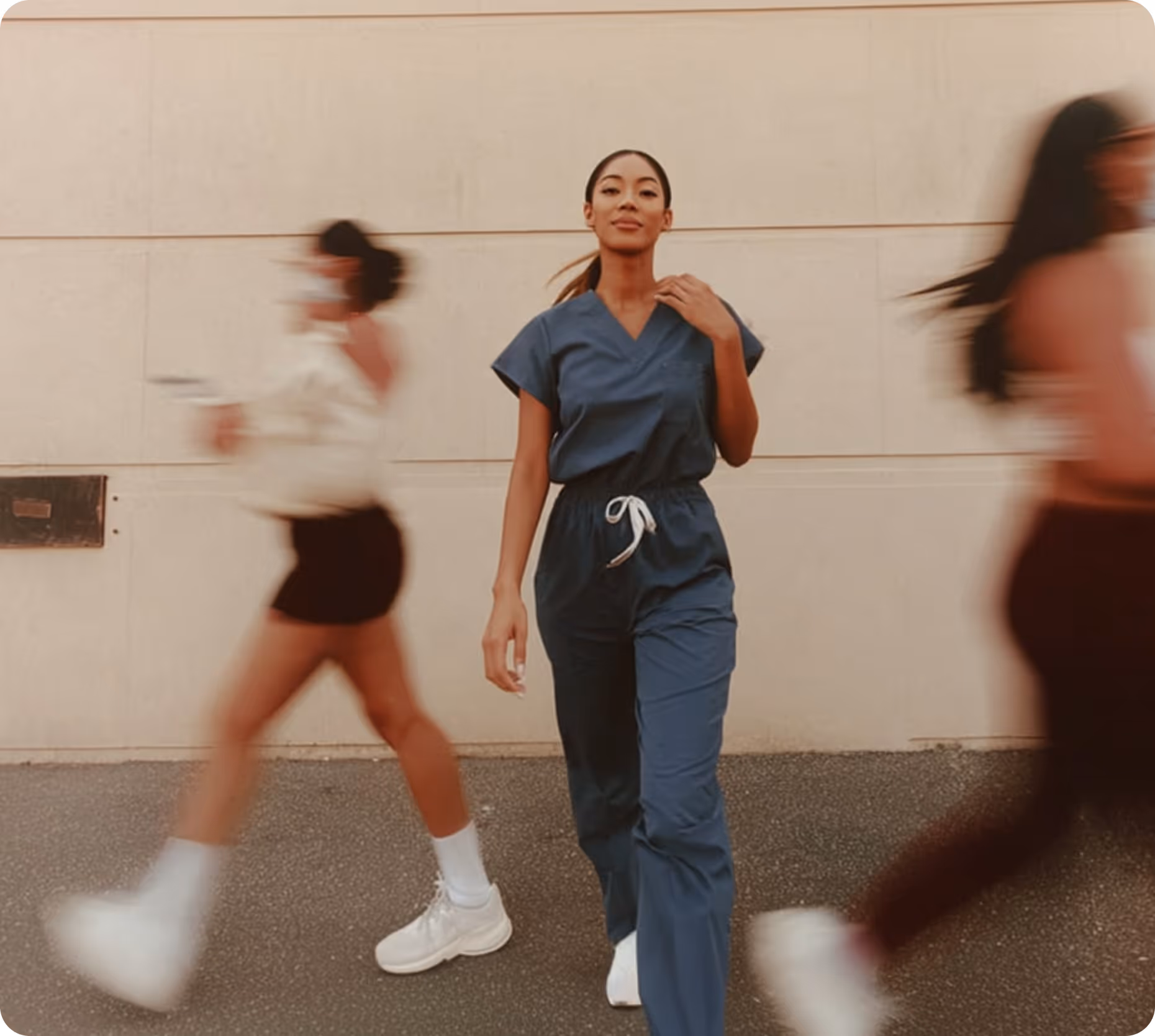 Woman in blue scrubs walking confidently with two blurred people passing by on either side.