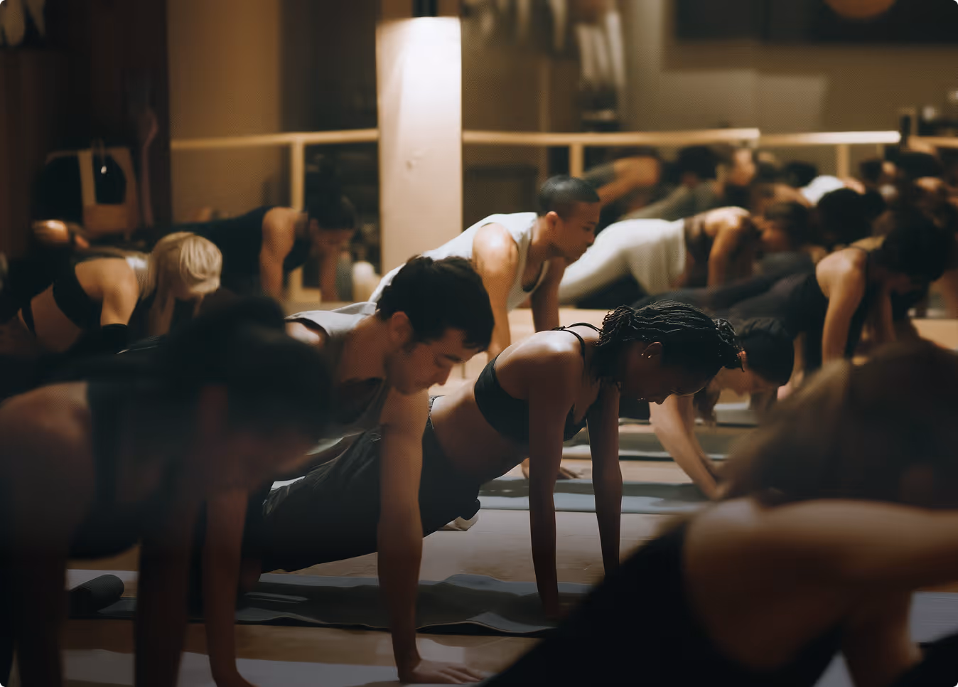 Group of people doing plank exercises on mats in a dimly lit fitness studio.