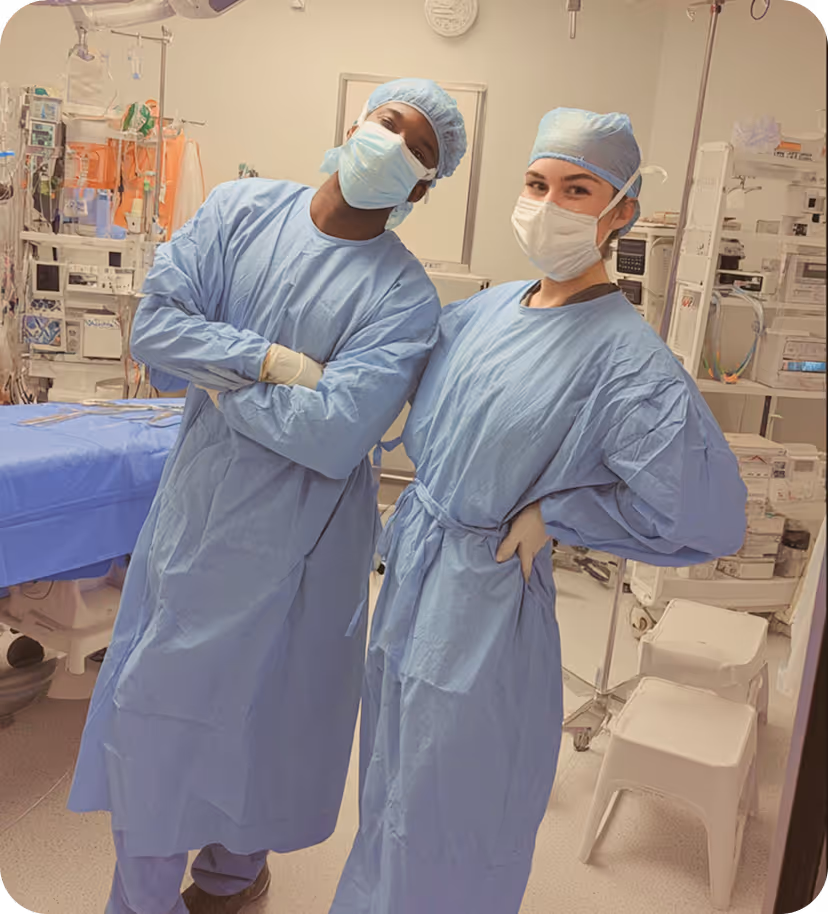 Two masked medical professionals in blue surgical gowns posing in an operating room.