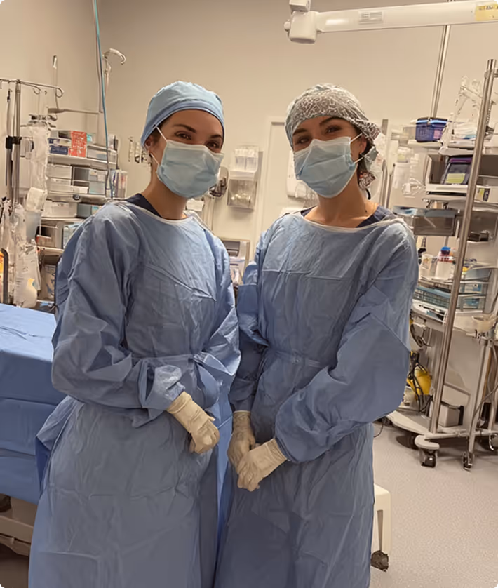 Two masked medical professionals in blue surgical gowns and gloves in a hospital room.