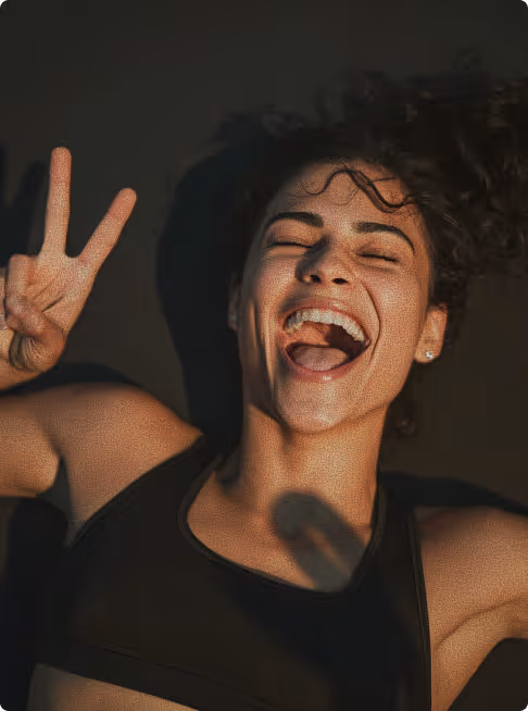 Close-up of a joyful woman with curly hair giving a peace sign and smiling with mouth open.