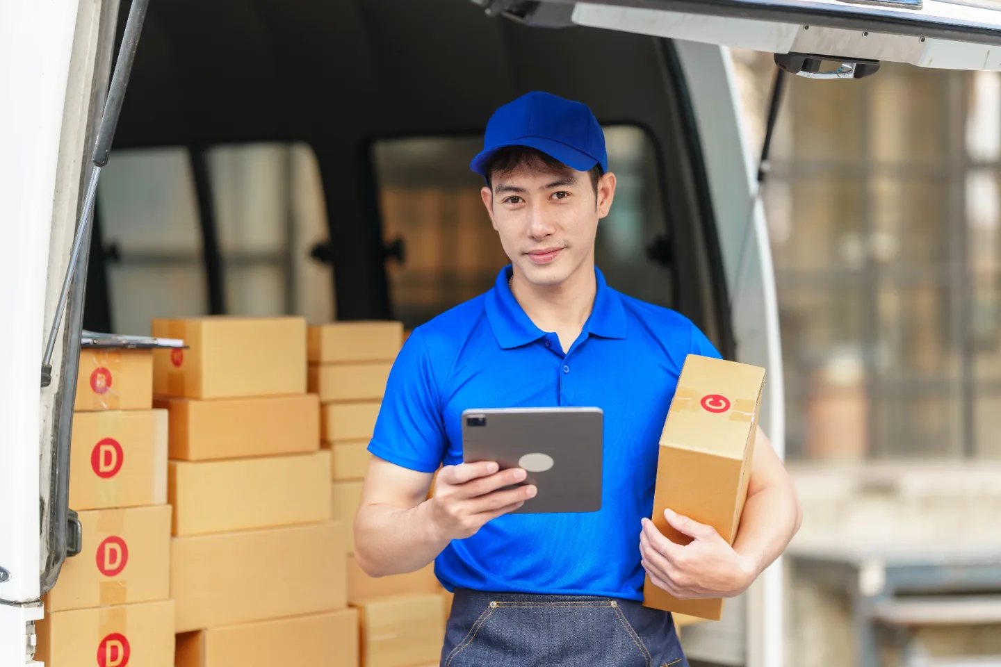 A delivery driver checking a handheld device at the open rear of a parcel van.