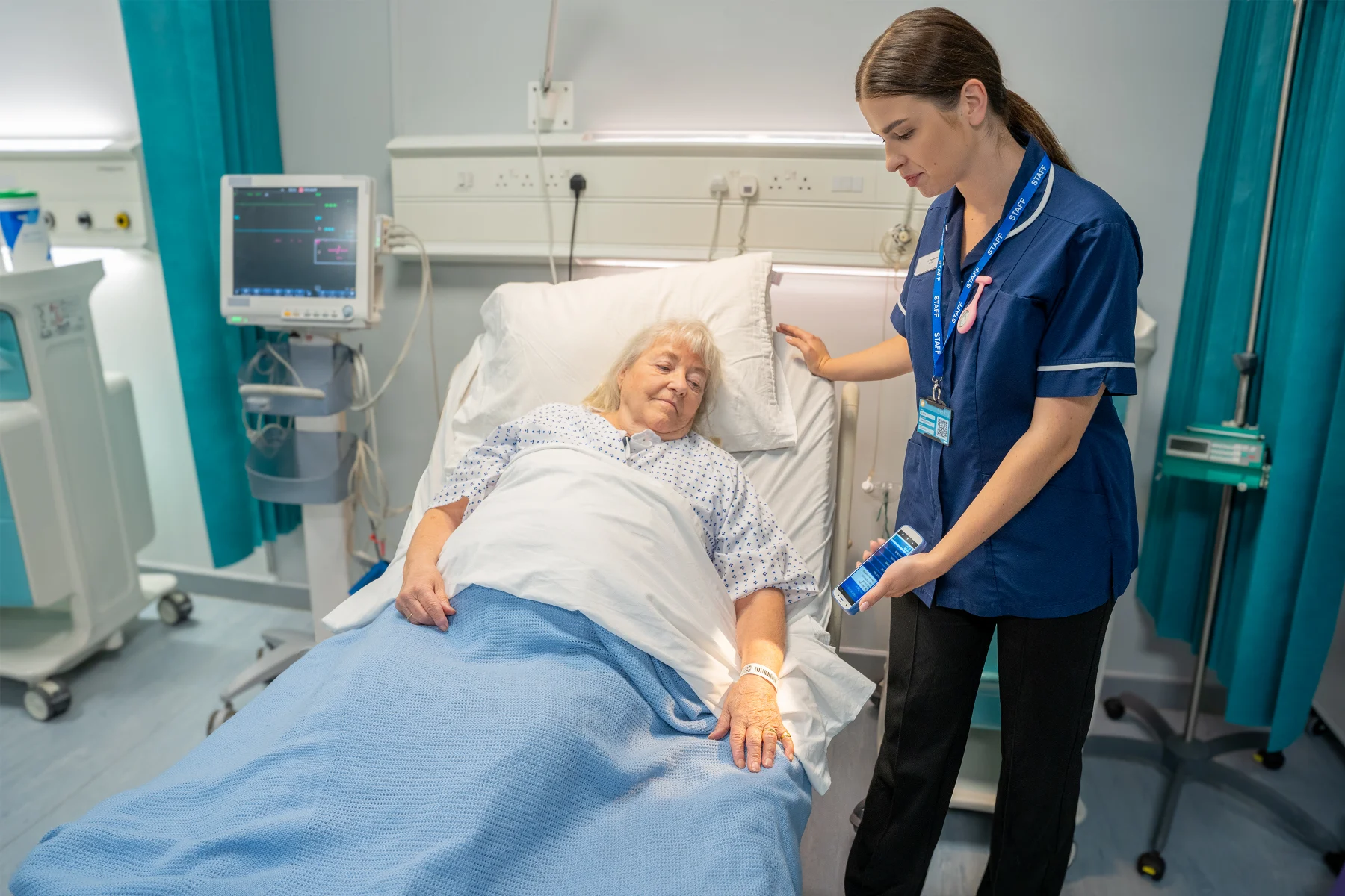 A nurse scanning a patient's wristband at the bedside with a handheld computer.
