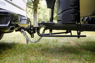 Close-up of a trailer hitch and weight distribution system connected to a vehicle on grass.