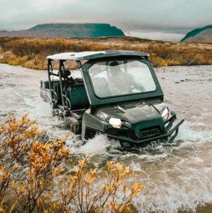Off-road utility vehicle driving through water in a rugged outdoor landscape with yellow foliage.