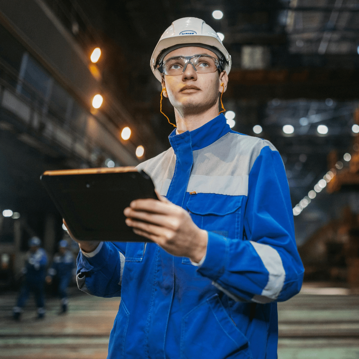 Field technician in a work uniform holding a tablet inside an industrial facility