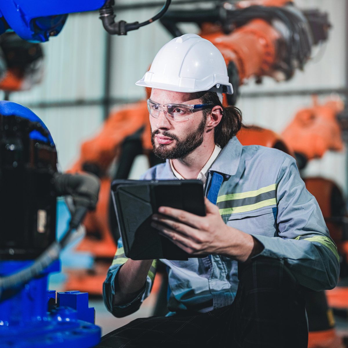 Factory technician holding a tablet while inspecting a robotic arm, using augmented reality work instructions