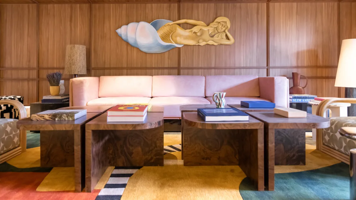 Living room with pink sofa, wooden coffee tables, colorful carpet, and a mermaid wall sculpture.