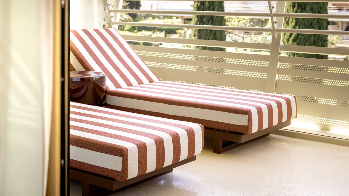 Two white and brown striped lounge chairs on a balcony with a round table between them.