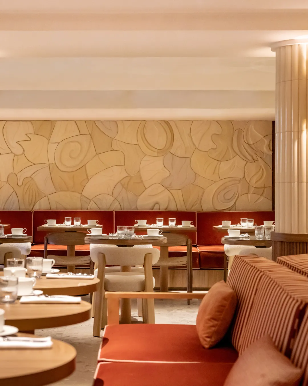Interior of a restaurant with wooden tables, chairs, red benches and abstract decorated wall.