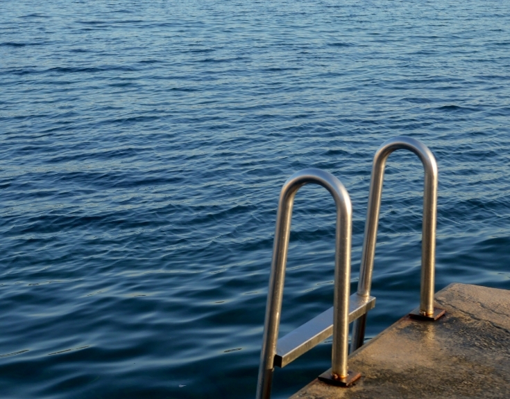 Metal ladder attached to a concrete dock at the edge of a calm and blue sea.