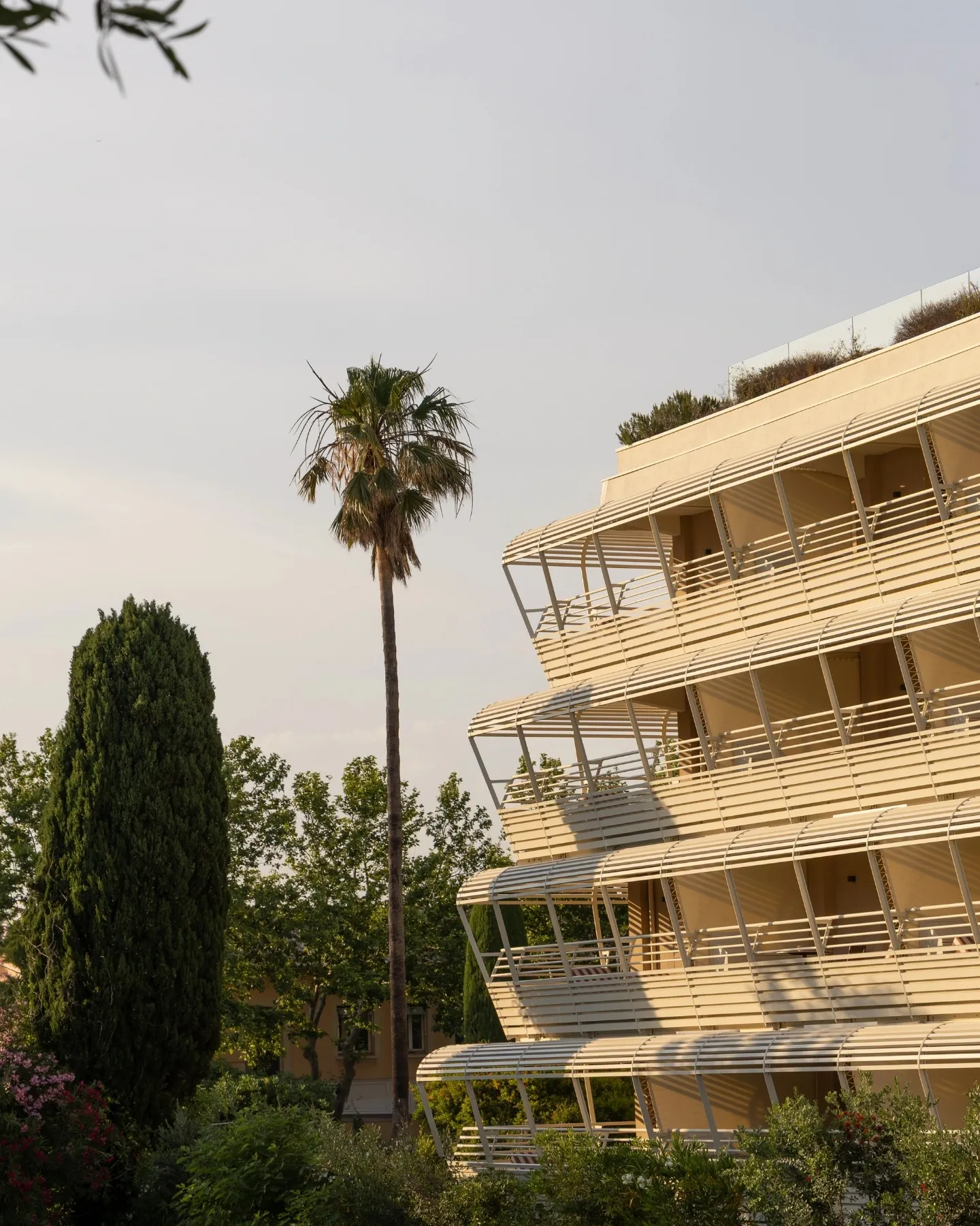 Façade de l'Hôtel Ventura, bâtiment moderne à balcons incurvés avec arbres et pelouse verte au coucher du soleil.