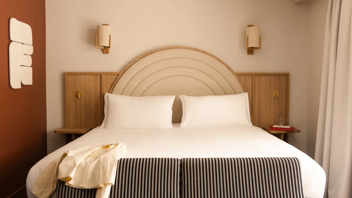 Chambre avec lit double, coussins blancs, tête de lit ronde beige et murs beige et marron.