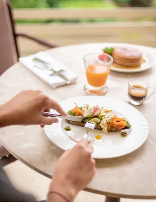 Breakfast on the terrace with salmon and avocado toast, orange juice, espresso, and pancakes on a marble table