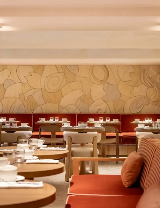 Elegant dining room set for service with round tables, terracotta banquettes, and a large sculpted wall featuring organic patterns