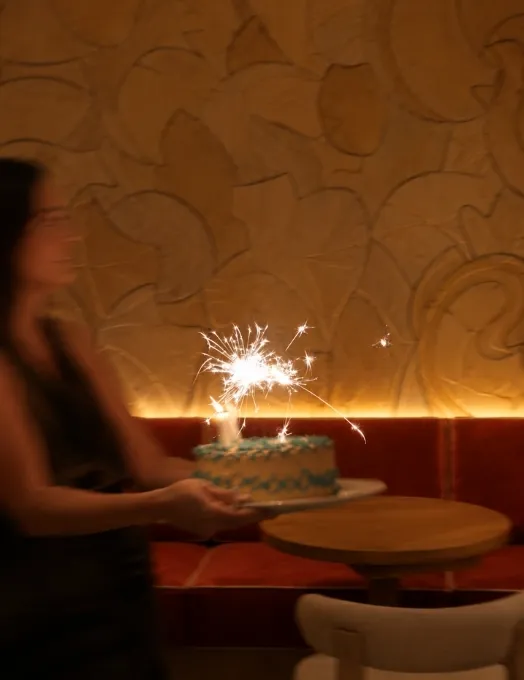 Waitress carrying a birthday cake with a sparkling sparkler in a dimly lit restaurant